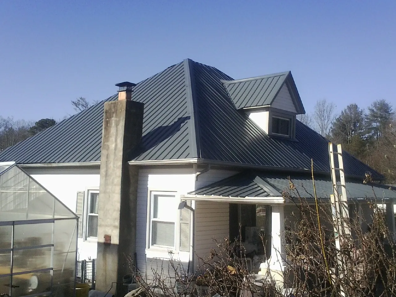 Dark blue standing seam metal roof on a white farmhouse with dormer — Slate & Tile Roof Repair by Roofing Brothers in Brookhaven