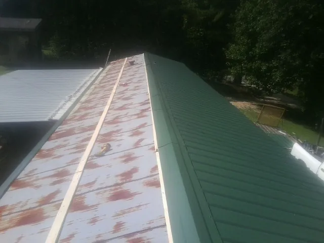 Old rusted panels beside newly installed green metal roofing — Wind Damage Roof Repair by Roofing Brothers in Brookhaven