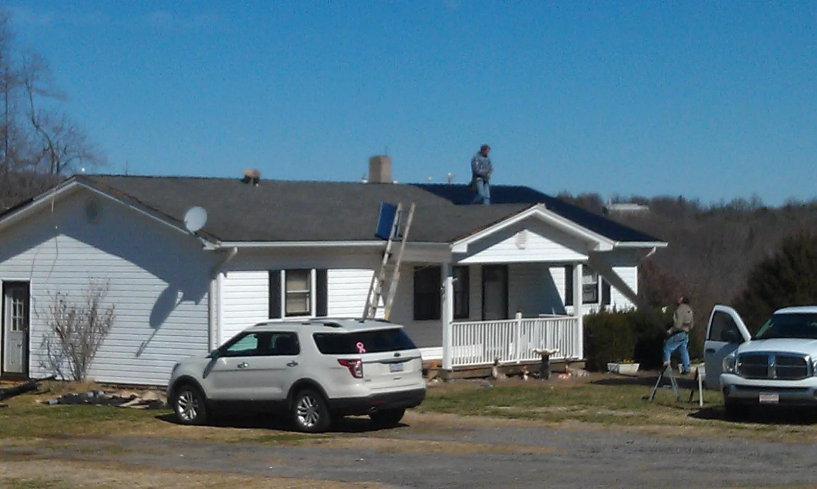 Roofers stripping shingles from a white ranch house roof in Brookhaven